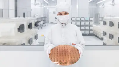 Employee in cleanroom suit holding a large silicon wafer in a modern semiconductor manufacturing facility.