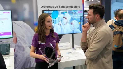 A Bosch expert talks to a customer. In her hand she holds a SiC wafer